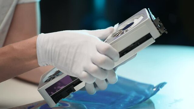 Closeup side view of unrecognizable repairman wearing latex gloves cleaning case of modern desktop video game card using wet wipes, during maintenance and service in electronics workshop, slow motion.