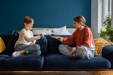 Two kids boy and girl friends play rock paper scissors hand game while sitting on sofa at home....