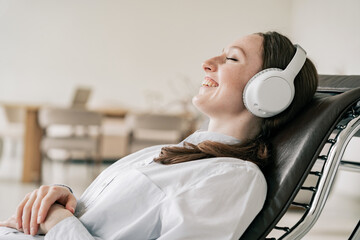 A woman listens to calm music or an audiobook with wireless headphones. Resting during a work break.