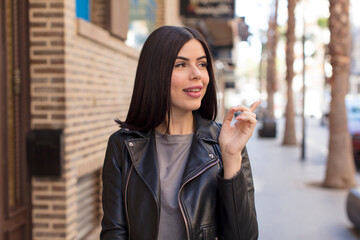 young pretty woman smiling cheerfully, feeling happy and pointing to the side and upwards, showing object in copy space