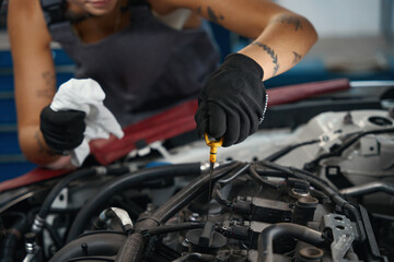 Car mechanic in protective gloves checks the oil level in car