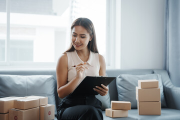 Using laptop, Portrait of pretty asian sme freelancer woman checking customer paid order on sofa after packing into cardboard box, online home small business, online influencer asia people.