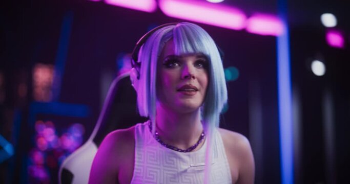 Smiling Cosplay Girl Talking to Her Online Friends on Desktop Computer While Sitting in Futuristic Cyberpunk Neon Home. Young Female Playing Internet Video Game with Other Players
