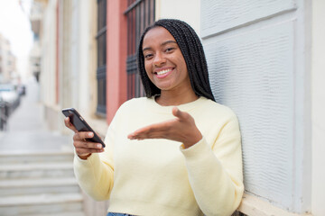 black afro woman smiling cheerfully, feeling happy and showing a concept. using a smartphone concept