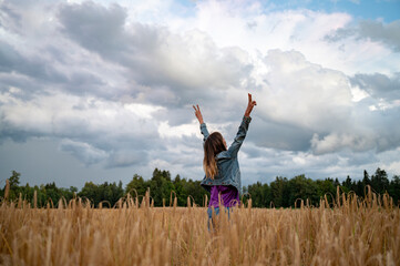 Joyful victorious young woman celebrating life as she stands with her arms raised high towards a...