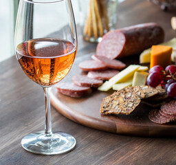 A glass of rose wine with a charcuteries board in soft focus in behind.