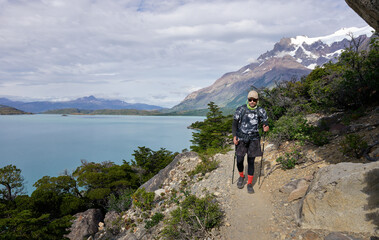 Fototapeta premium Mature hiker walking on a trail with a view of the lake and mountains in the background in Torres del Paine National Park