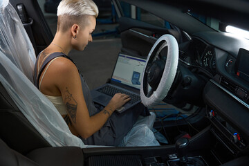 Car mechanic in work overalls conducts computer diagnostics of car
