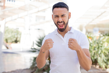 Fototapeta premium young handsome man shouting aggressively with annoyed, frustrated, angry look and tight fists, feeling furious