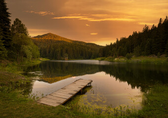 Fototapeta na wymiar Small lake and pier at sunset.Mountain lake and pine forests.