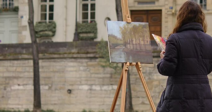 Female street art painter has some sketch practice with Paris city landscape. Experienced European woman artist draws new painting near the river. Painter and her lifestyle hobby leisure