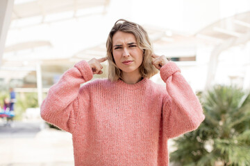 pretty woman looking angry, stressed and annoyed, covering both ears to a deafening noise, sound or...