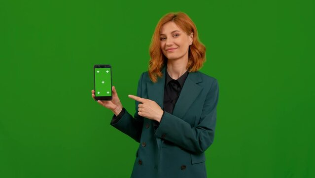 Woman pointing to mock up smartphone with aproval over green screen background. Sell advertising a product or app on chroma key phone screen.