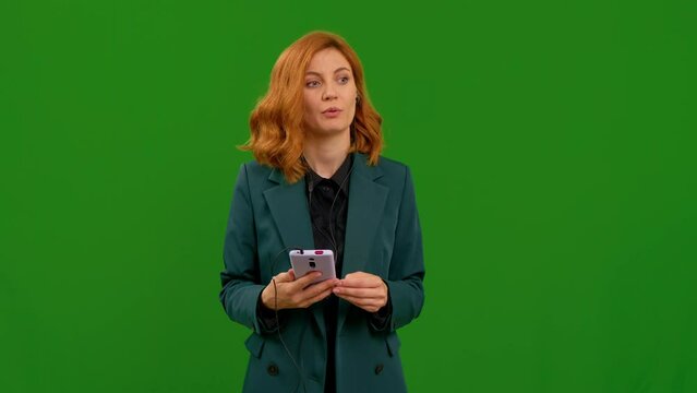 Serious woman wearing headset while working in freelance. Support service operator helpline having talk with client or colleague. Female on green chroma key background.