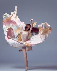 Beautiful ballerina dancing elegant, grace movement with flying fabric over grey studio background. Dancer in motion © Lustre Art Group 