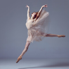 Young and incredibly beautiful ballerina wearing tulle dress jumping gracefully over grey studio...