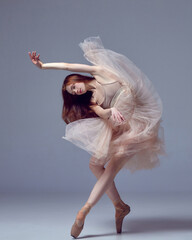 Sensual red haired ballerina wearing tulle dress dancing with emotions over grey studio background....