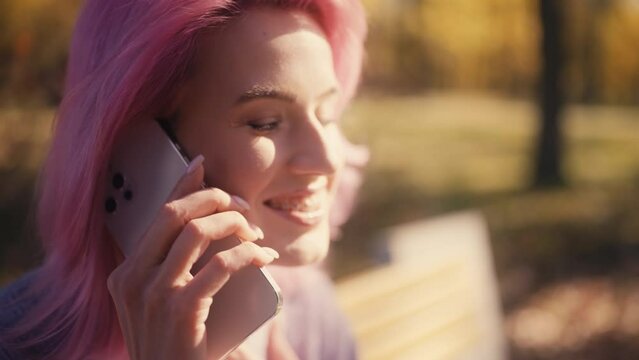 Young pink-haired woman talking on phone outdoors, having fun during free time