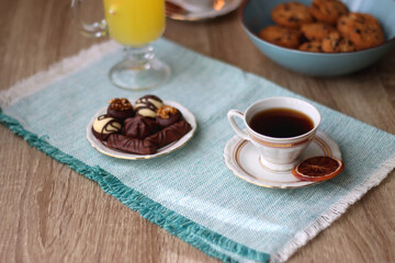 Plate of chocolate pralines, bowl of cookies, cups of tea, glasses of juice and lit candles on the table. Selective focus.