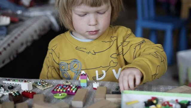 a small child in the playroom plays with toys and sorts through the beads. Boy playing on the couch in a pile of toys