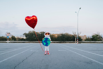 Girl with earth cut out and heart balloon standing in parking lot