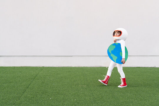 Girl wearing astronaut costume holding earth cut out walking on grass
