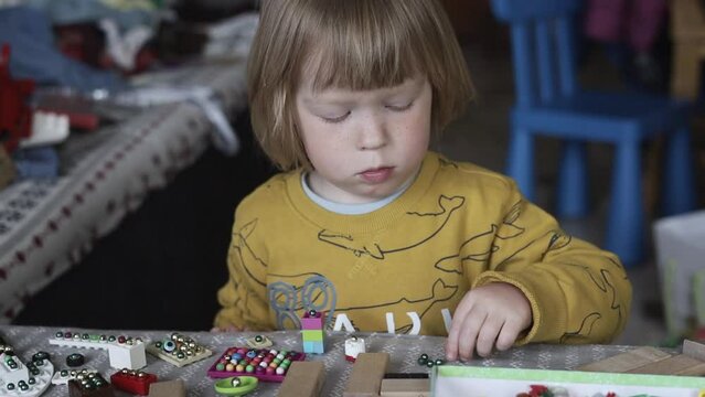 a small child in the playroom plays with toys and sorts through the beads. Boy playing on the couch in a pile of toys