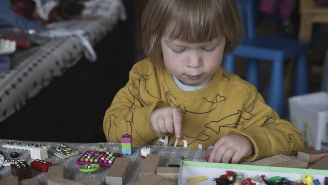 a small child in the playroom plays with toys and sorts through the beads. Boy playing on the couch in a pile of toys