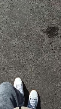 Man's feet steps on the asphalt in white sneakers close up. First-person view walking. Vertical footage.