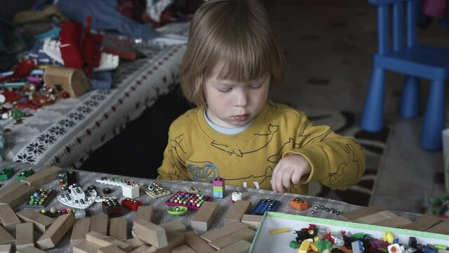 a small child in the playroom plays with toys and sorts through the beads. Boy playing on the couch in a pile of toys