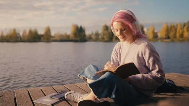 Creative woman in headphones writing notes in her diary, spending time alone