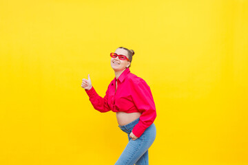 Fototapeta na wymiar A smiling pregnant woman in a pink cotton shirt and jeans gently holds her pregnant belly. Posing for the camera. Concept of easy and happy pregnancy.