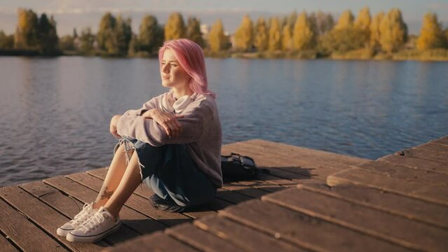 Sad young woman with pink hair sitting by the river alone, problems, introvert
