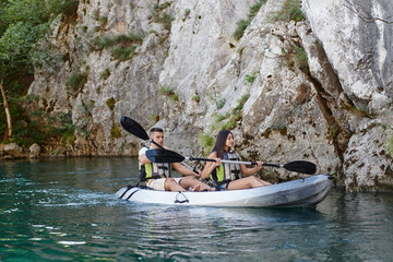 A young couple enjoying an idyllic kayak ride in the middle of a beautiful river surrounded by forest greenery