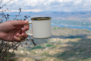 Man holding coffee mug for camping in nature, mug, tea mug, metal mug for hot drinks, enamel kitchen utensils.