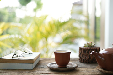 Earthenware teapot glasses and tea cup and notebooks and cactus pot on wooden table