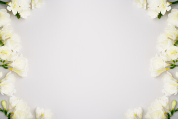 Fototapeta na wymiar Spring floral frame. White flowers on light grey background. Spring holiday composition. Fresh freesia template for product advertising or sale. Top view, flat lay, copy space. Blooming layout.