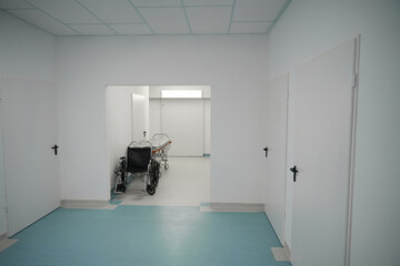Mobile postoperative bed and wheelchair are located in bright hospital corridor
