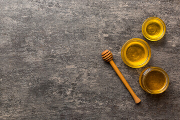 Glass jar of honey with wooden drizzler on colored background. Honey pot and dipper high above. Top view copy space