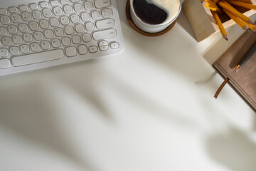 Top view of keyboard, coffee cup and stationery on white working desk.