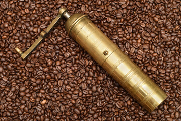 Old golden manual coffee grinder lying down on the heap of fresh roasted coffee beans 