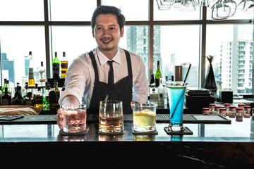 Smiling young smart Bartender man doing cocktails in rooftop bar and restaurant