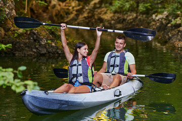 A young couple enjoying an idyllic kayak ride in the middle of a beautiful river surrounded by forest greenery