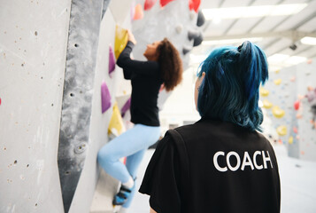 Woman On Climbing Wall At Indoor Activity Centre Receiving Personal Lesson From Coach