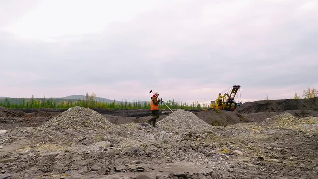 Male surveyor is carrying the prism pole tool at the quarry. Using the modern mine surveying pole tool to analyze the area. Worker is searching for valuable metals with a surveying pole tool
