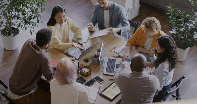 Top view of business partners diverse group talking sitting around table in board room in office. Communication and corporate activity concept.