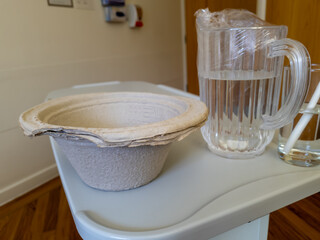 A sickness container and some water by the side of the hospital bed in a patient's recovery room.