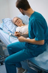 Fototapeta premium Nurse sits on a bed next to an elderly patient