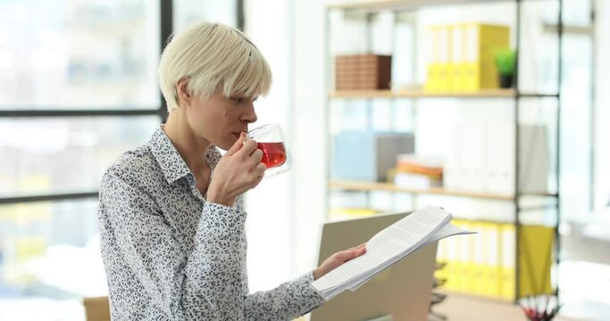 Woman reads business report and holds tea cup standing in company office. Business lady prepares for corporate meeting during work break