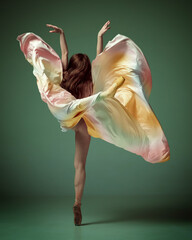 Back view of one charming ballerina, ballet dancer wearing fancy colorful dress posing on tiptoe over dark green studio background. Aesthetic of movement © Lustre Art Group 